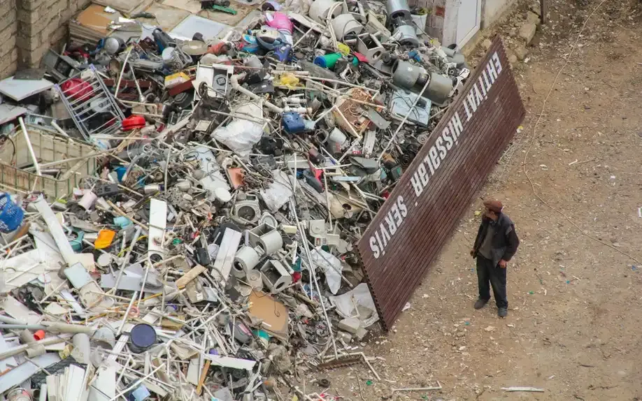 A worker beside a large bay of mixed scrap metal during a site clean-up.